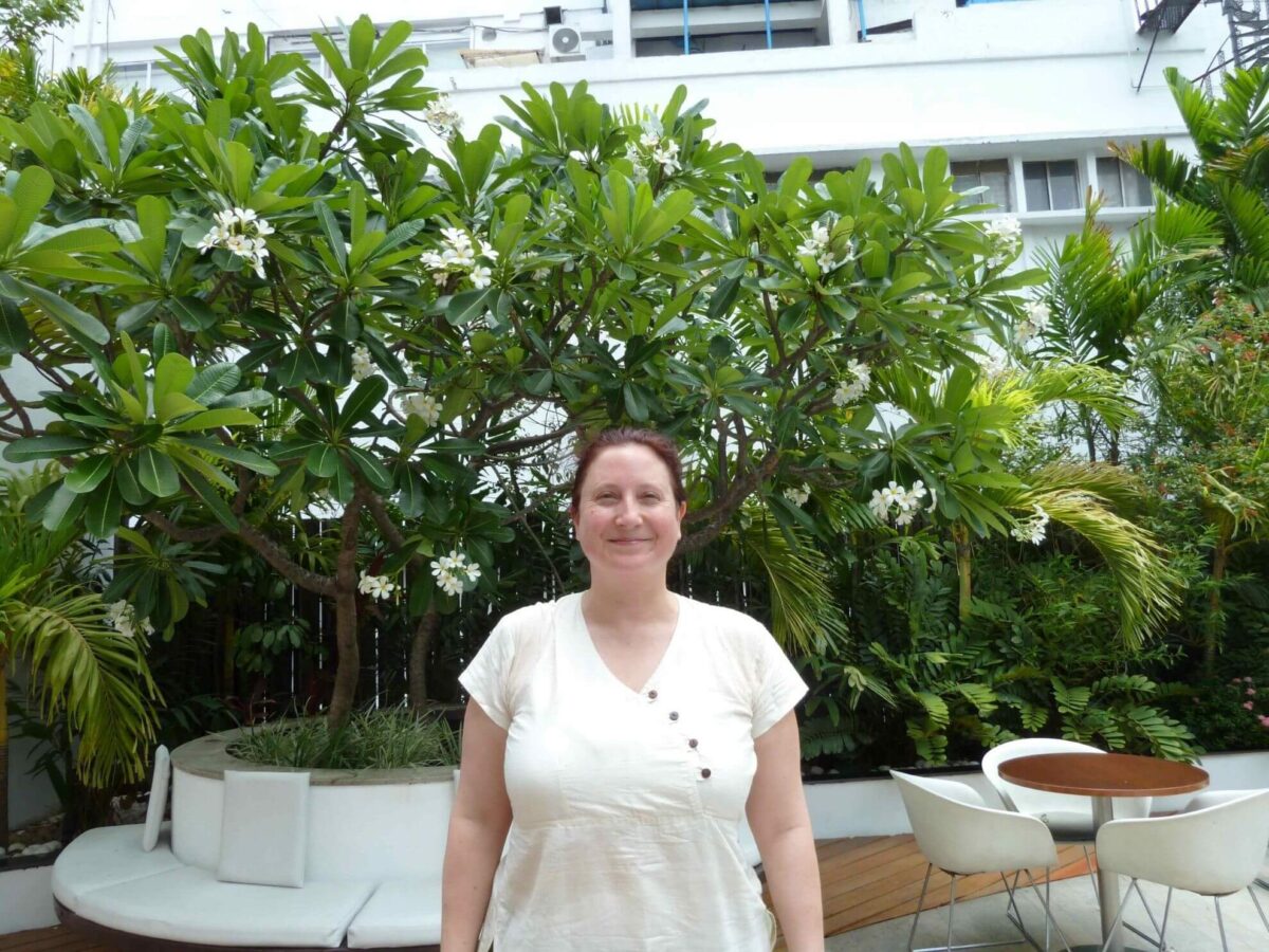 Sylvie Beauvais in front of green tropical trees with white flowers - About Sylvie Beauvais